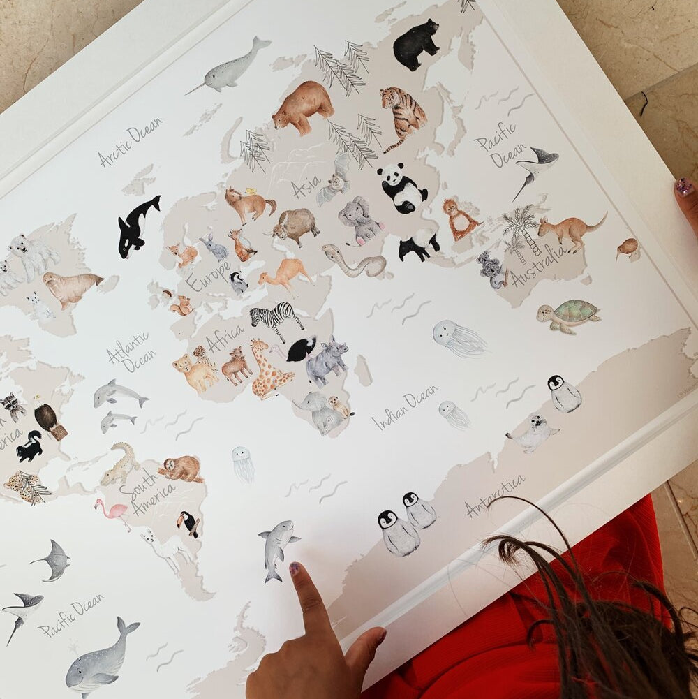 A person pointing at a world map fine art print featuring watercolor illustrations of animals representing different countries.